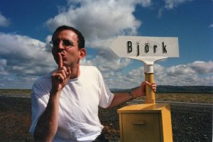 Richard in white t-shirt holding onto a road sign(?) reading Bjork