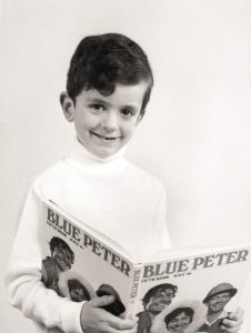 Black and white photo of Richard as a kid. Smiling in a white polo neck holding the Blue Peter Annual - Fifth book - look up the year - I did actually, and it's 1968
