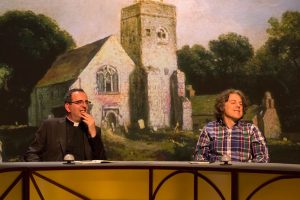 Richard on the set of Qi with Alan Davies. Illustration of old Church in background.