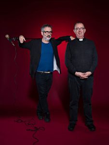 David Baddiel (with mic & stand across his shoulders) looking at Richard. Red background